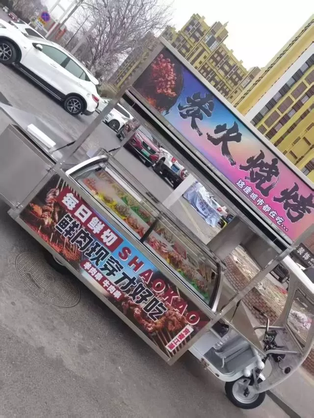 烧烤三轮餐车，不锈钢车身，带玻璃展示柜+操作台，顶部有“炭火烧烤”广告灯箱，配L…